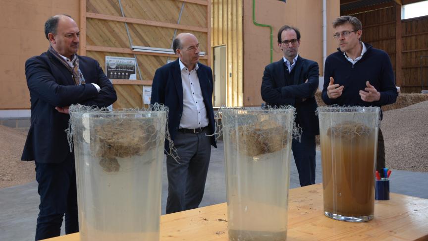 Willy Borsus, Olivier de Wasseige, Chuck de Liedekerke et Nicolas Verschuere (de gauche  à droite) observent les résultats du « slake test »: dans le récipient de droite, la motte  issue d’une parcelle intensive se désagrège rapidement tandis que les mottes  « régénérative » et « forestière » ne se délitent que très peu.